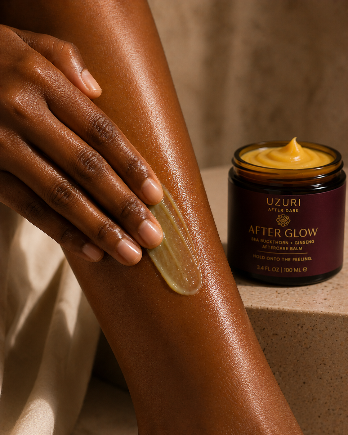 Person applying Uzuri After Glow balm to their leg with a jar of the product in the background.