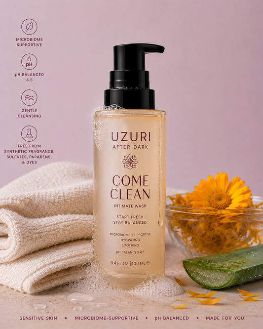 Uzuri After Dark Come Clean intimate wash bottle with a towel and flowers on a pink background